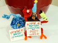 A photograph of Finn, a pompom and pipecleaner person with an anglerfish for a head, and Bentley, a robot with a jar holding a clownfish for a head. They sit next to each other, and both hold signs saying, "Vote Bentley Finnegan for Guest of Honor."