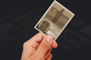 A hand holding an aged baseball card, the card depicts a blocky squid wearing a wizard hat