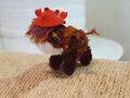 A photograph of Zora Duffy, a small fluffy cow made of pompoms and pipecleaners. She wears a crab bucket hat.