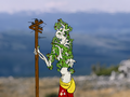 ID: An image of Melton Telephone, an animate whitebark pine convoluted into humanoid shape, standing on a hill. They are beckoning towards the viewer while leaning on a staff made from a disconnected telephone pole with their other arm.